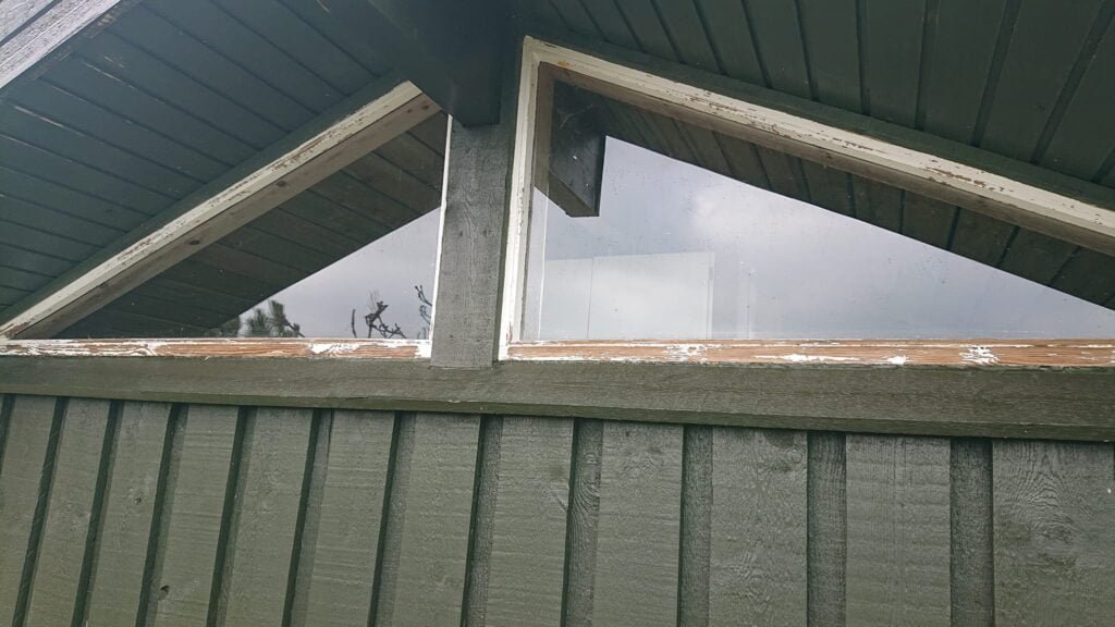 Grønt træhus med trekantede vinduer under tag.